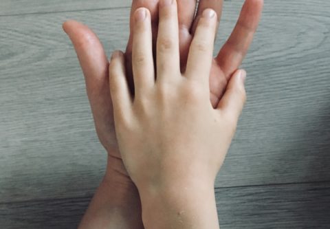 Lapsen käsi lepää aikuisen kämmenellä.