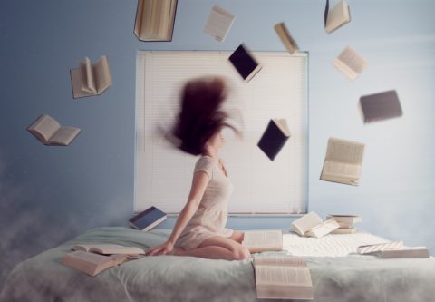 Henkilö istuu vuoteella ja heittää lukuisia kirjoja ilmaan.