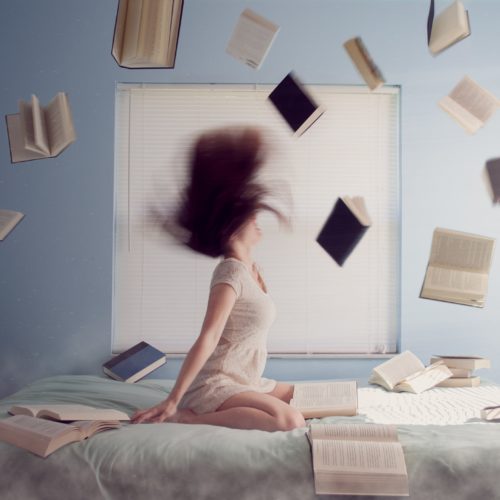 Henkilö istuu vuoteella ja heittää lukuisia kirjoja ilmaan.