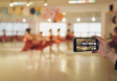 Tanssijat tanssivat harjoitussalissa ja joku kuvaa kännykällä harjoituksia.