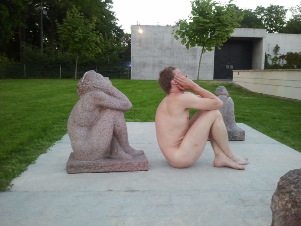 Antti istuu patsaan kanssa alasti ulkona pihalla. Hän katsoo taivaalle samassa asennossa kuin patsas.