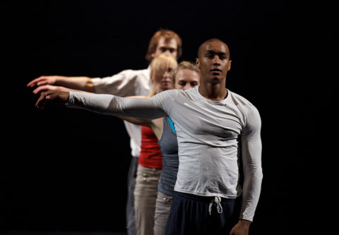 Neljä tanssijaa seisoo jonossa oikea käsivarsi kohotettuna.