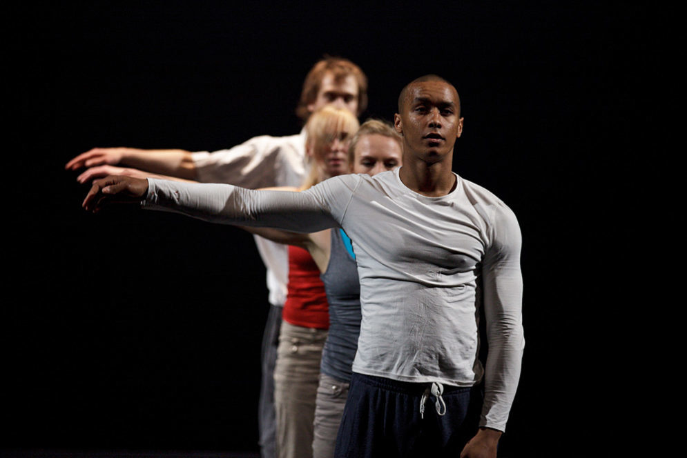 Neljä tanssijaa seisoo jonossa oikea käsivarsi kohotettuna.