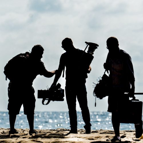 Kolmen hengen kuvausryhmä valmistautuu kuvauksiin meren rannalla.