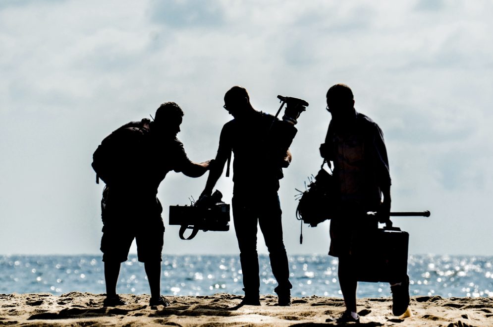 Kolmen hengen kuvausryhmä valmistautuu kuvauksiin meren rannalla.