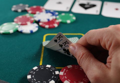 Pelipöydässä pelataan rahasta ja pelaaja kurkkaa korttejaan, jotka ovat kuningaspari.