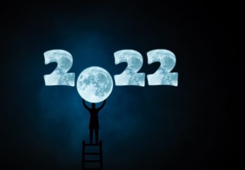 Vuosiluvussa 2022 on nollan paikalla kuu, jota henkilö kurkottaa tikkailta.