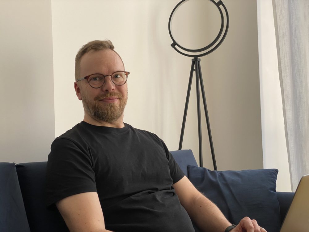 Antti Kaarlela nojaa tummansiniseen sohvaan mustassa t-paidassaan.