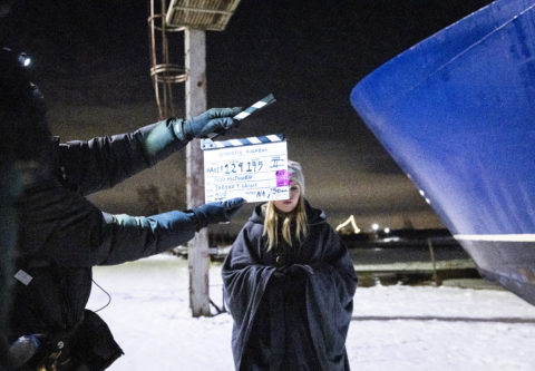 Venesatamassa, lumen keskellä elokuvatyöntekijä näyttää klaffia vaaleatukkaisen näyttelijättären edessä. Oikealla näkyy sinistä venettä.