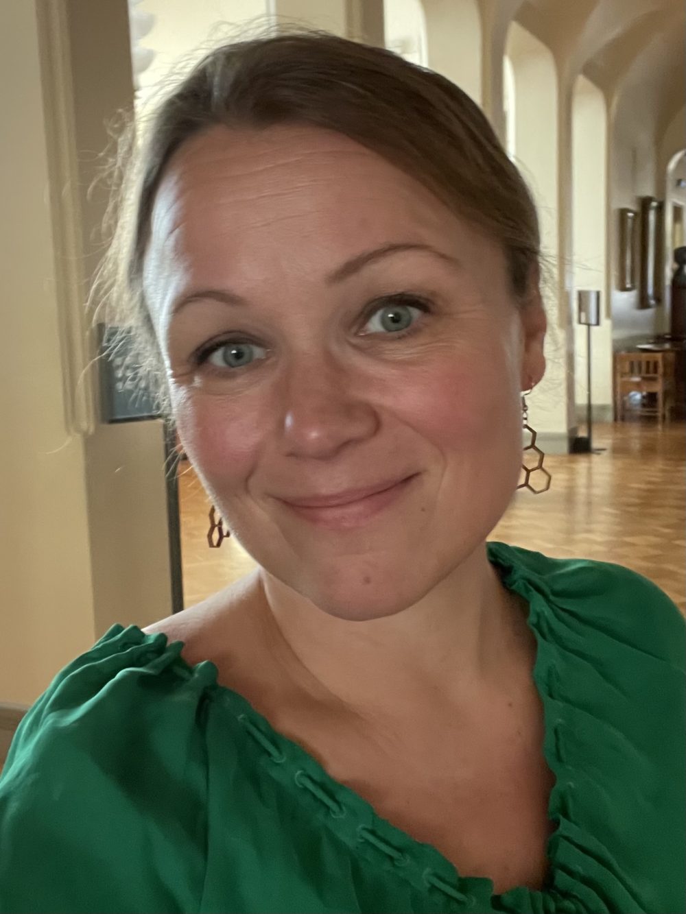 Suomen Kansallisteatterin myynti- ja markkinointipäällikkö Marika Agarth katsoo kameraan kansallisteatterin lämpiössä vihreä pusero päällään.